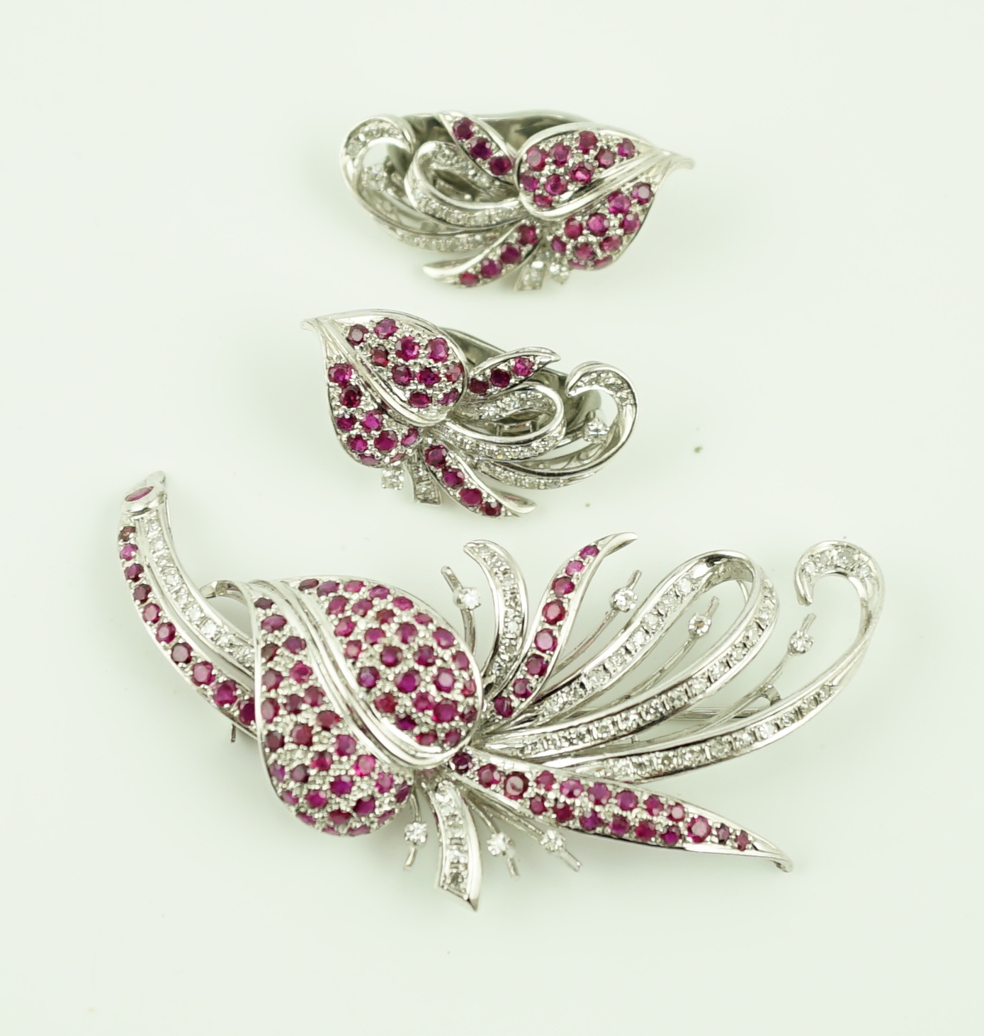 A suite of platinum?, diamond and ruby set cluster jewellery, comprising a spray brooch and pair of matching ear clips